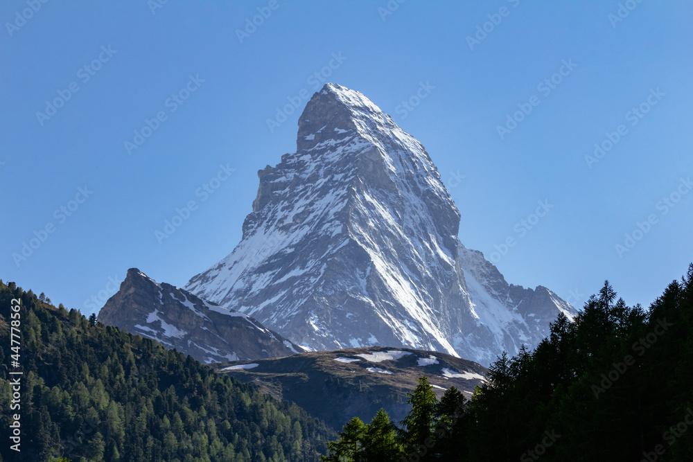 View of iconic Matterhorn mountain summit with snow from Zermatt valley, with green vegetation, trees and wooden cottages, Valais, Swiss Alps, Switzerland