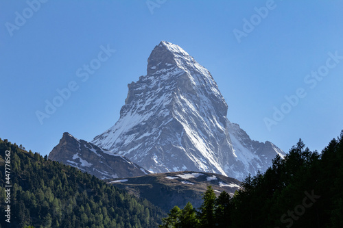 View of iconic Matterhorn mountain summit with snow from Zermatt valley, with green vegetation, trees and wooden cottages, Valais, Swiss Alps, Switzerland