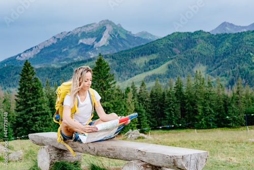 Girl traveler with yellow backpack sitting on a bench with a paper map.
