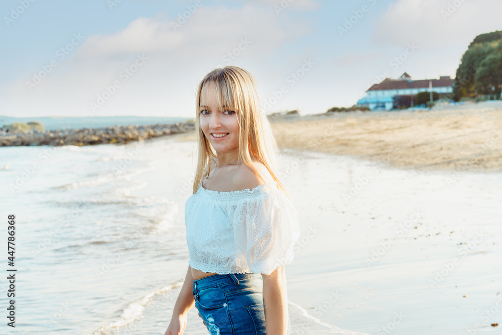 Portrait of happy smiling woman in white top and jeans shorts enjoying the moment during a walk on the seaside beach. Summer holidays, vacation. Simple pleasure. Copy space. Portrait of happy smiling woman in white top and jeans shorts enjoying the moment during a walk on the seaside beach. Summer holidays, vacation. Simple pleasure. Copy space.