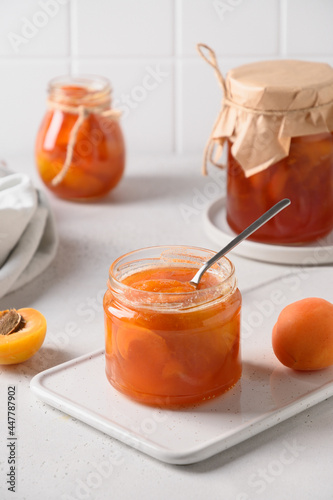 Apricot jam in open glass jar with fruits on white background. Summer harvest and canned food for winter. Tasty dessert. Close up.