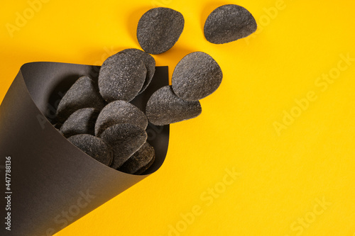 black potato chips in a black paper package on a yellow background  copy space