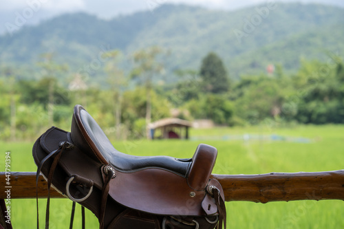 Closeup shot of a horse saddle hanging on a wooden fence on a field
