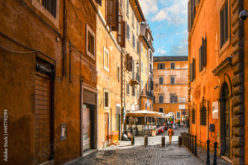 A colorful empty alley leading to a sidewalk cafe and small piazza in the historic center of Rome, Italy