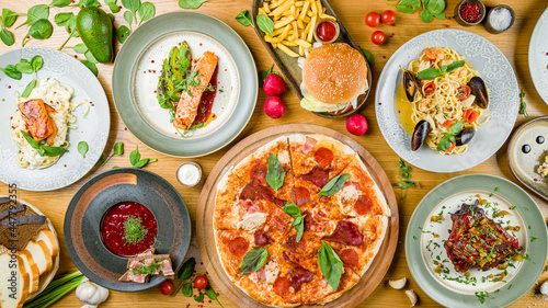 Italian meat pizza, salmon steak with avocado, spaghetti with shrimps and mussels, burger with meat, pork reabs bbq, borsht, bread, spaghetti with salmon top view on wooden table