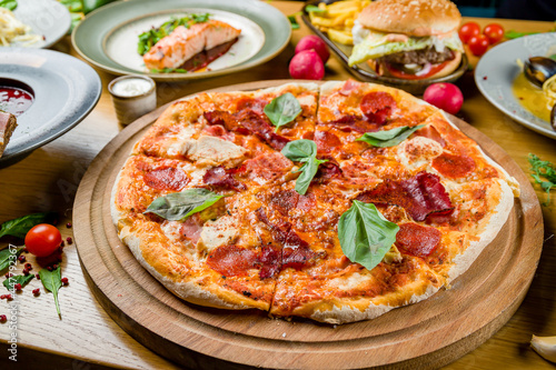 Italian meat pizza with chicken, ham, basil and cheese on the board on wooden table
