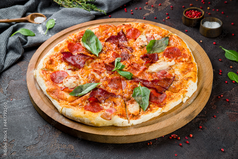 Italian meat pizza with chicken, ham, basil and cheese on the board on dark concrete table