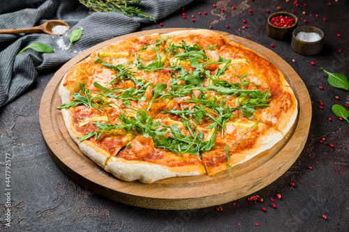 Pizza with arugula and shrimp on the board on dark concrete table