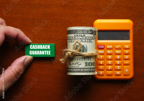 A pictire of hand holding green wood written cashback guarantee, fake money and calculator. It’s a credit benefit that refunds the cardholder a small percentage of the amount spent on each purchase photo