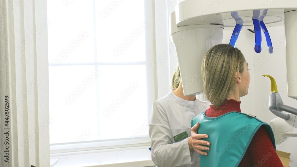 Doctor to take a image 3d scanner tomography of teeth and jaw in modern laboratory dental clinic. Female nurse shows the patient woman an x-ray machine 3d digital scanner. Computer dental diagnostics. Doctor to take a image 3d scanner tomography of teeth and jaw in modern laboratory dental clinic. Female nurse shows the patient woman an x-ray machine 3d digital scanner. Computer dental diagnostics.