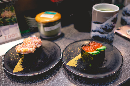 Two black plates with sushi pieces with fish, crab, masago (fish eggs) and cucumber, and cup of matcha green tea at restaurant in Tokyo, Japan photo