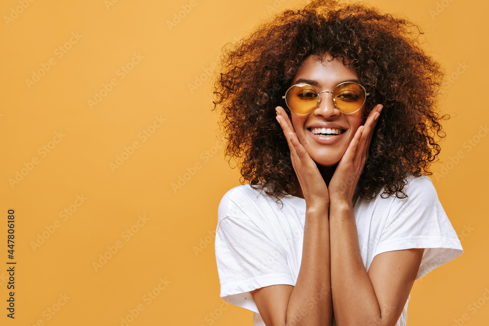 Lovely woman in light outfit smiling on yellow background. African girl in bright sunglasses looks into camera on isolated backdrop.. Lovely woman in light outfit smiling on yellow background. African girl in bright sunglasses looks into camera on isolated backdrop..