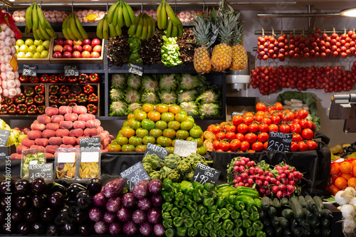 Colorful market counter with large assortment of fruits and vegetables. Price tags with product names in Catalan