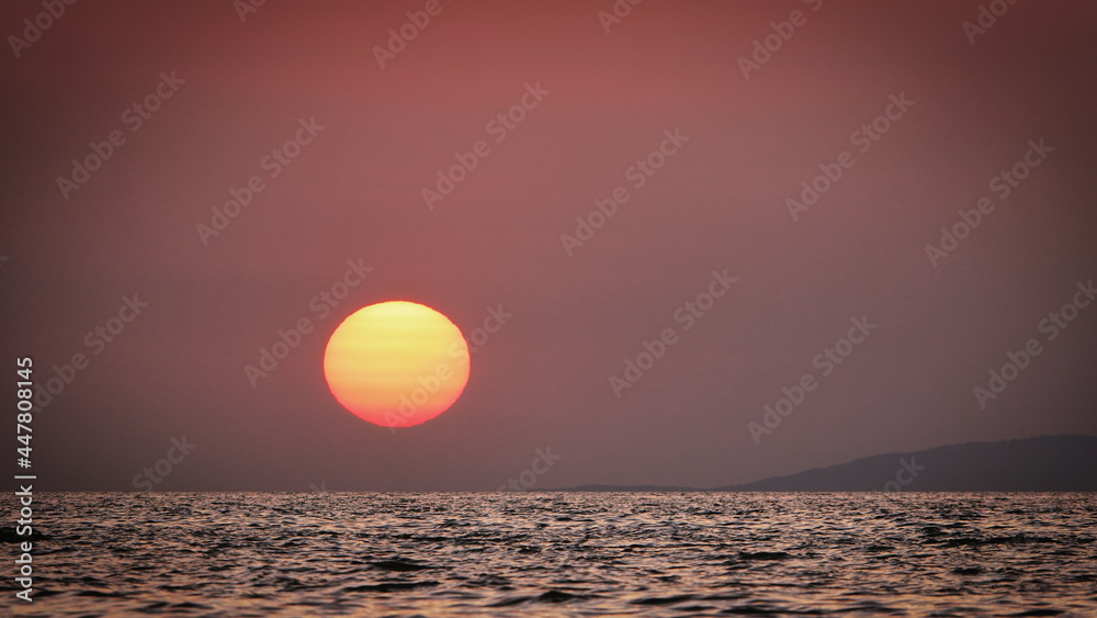 Orange sunset over the sea in Gökçeada and the silhouette of Samothrace island across it