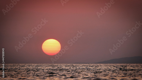 Fototapeta Naklejka Na Ścianę i Meble -  Orange sunset over the sea in Gökçeada and the silhouette of Samothrace island across it