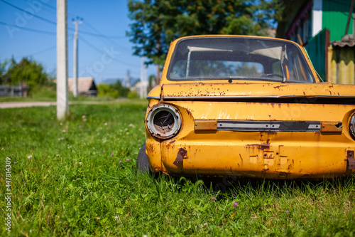 Old yellow wrecked car in vintage style. Abandoned rusty yellow car. Close-up of the headlights of the front view of a rusty, broken, abandoned car near the house.