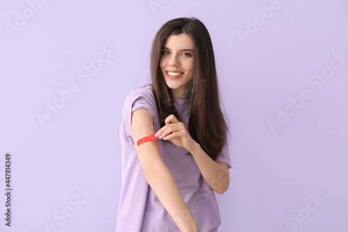 Young woman removing medical patch against color background