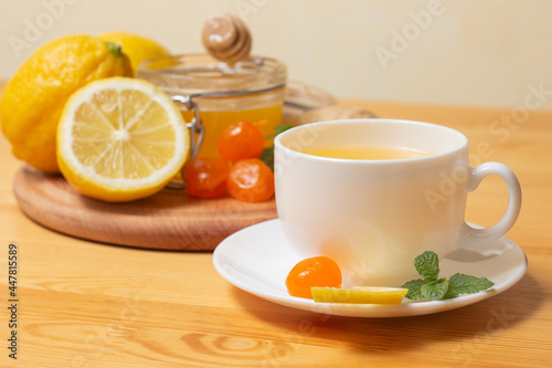 Ginger tea with mint and lemon. Healthy and hot drink. Liquid honey in honey-jar. White cup on wooden background. Selective focus.