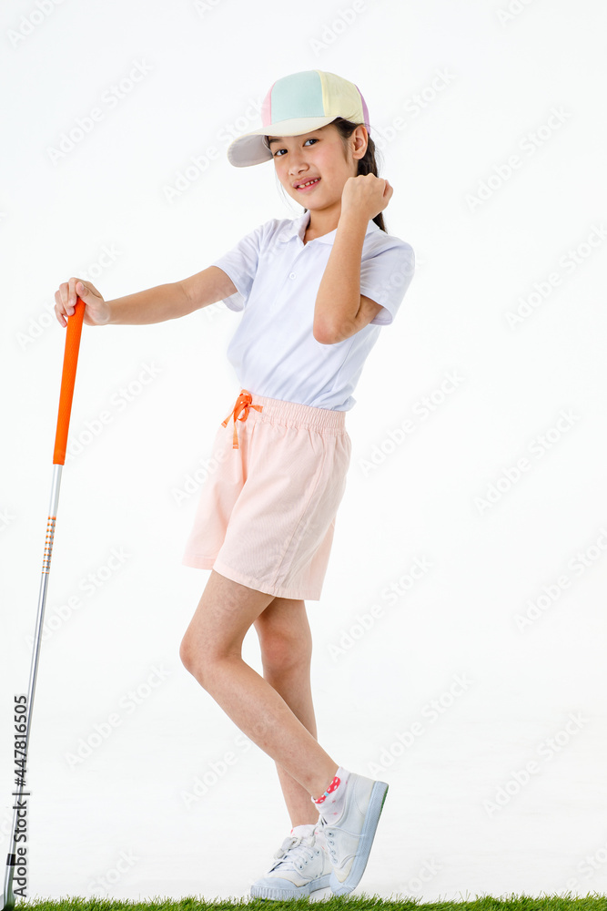Fototapeta premium Portrait isolated studio shot of pretty cute little Asian golfer in sport uniform and colorful cap stand on green grass posing put hands on orange grip of golf club driver in front white background