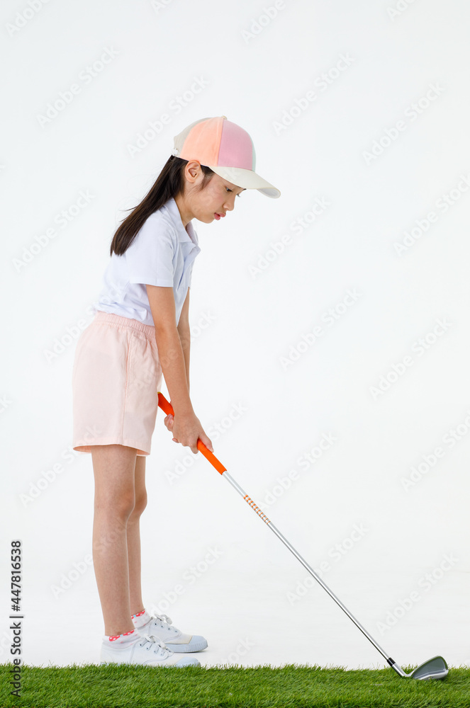 Portrait isolated studio shot of Asian little professional girl golfer in sport cloth uniform holding golf club driver in hands ready to drive and hit ball on green grass in front of white background Portrait isolated studio shot of Asian little professional girl golfer in sport cloth uniform holding golf club driver in hands ready to drive and hit ball on green grass in front of white background