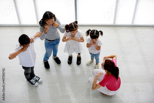 Top view shot of Asian female primary education school dancing teacher sit teach group of little boy and girls to perform crying posture in happy fun private kindergarten acting class in studio room