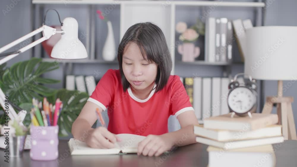 school girl pupil studying at home sitting at desk. Smart cute kid primary school student writing in exercise book thinking homework, learning at table. school girl pupil studying at home sitting at desk. Smart cute kid primary school student writing in exercise book thinking homework, learning at table.