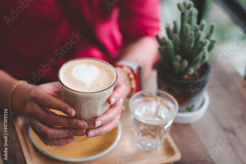 Female s hand holding cup of coffee on wooden table.