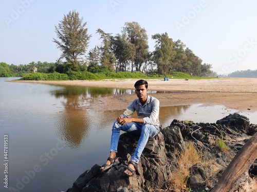 person sitting on a rock with beautiful lake in background, a young men enjoying view of nature. Smiling pretty young man. 