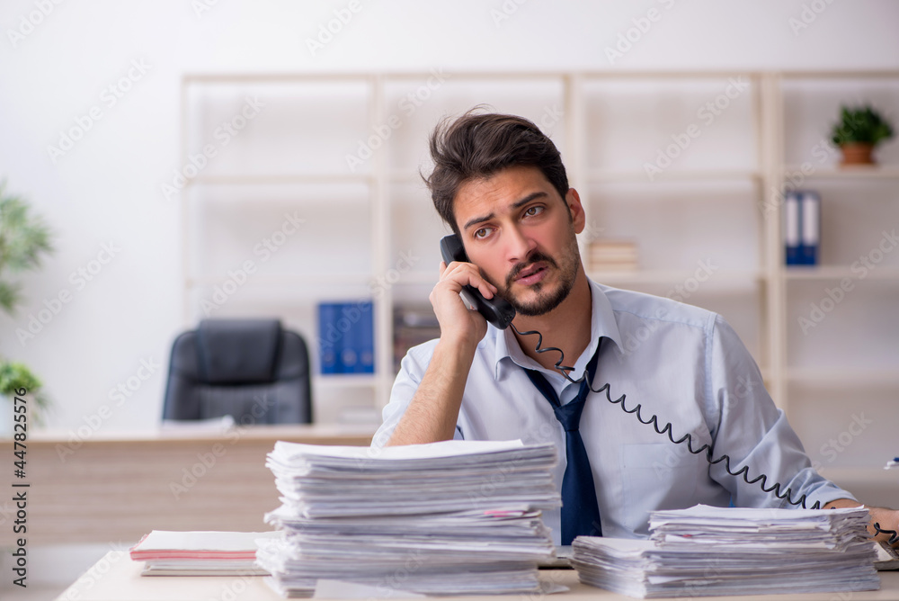 Young male employee unhappy with excessive work in the office Young male employee unhappy with excessive work in the office