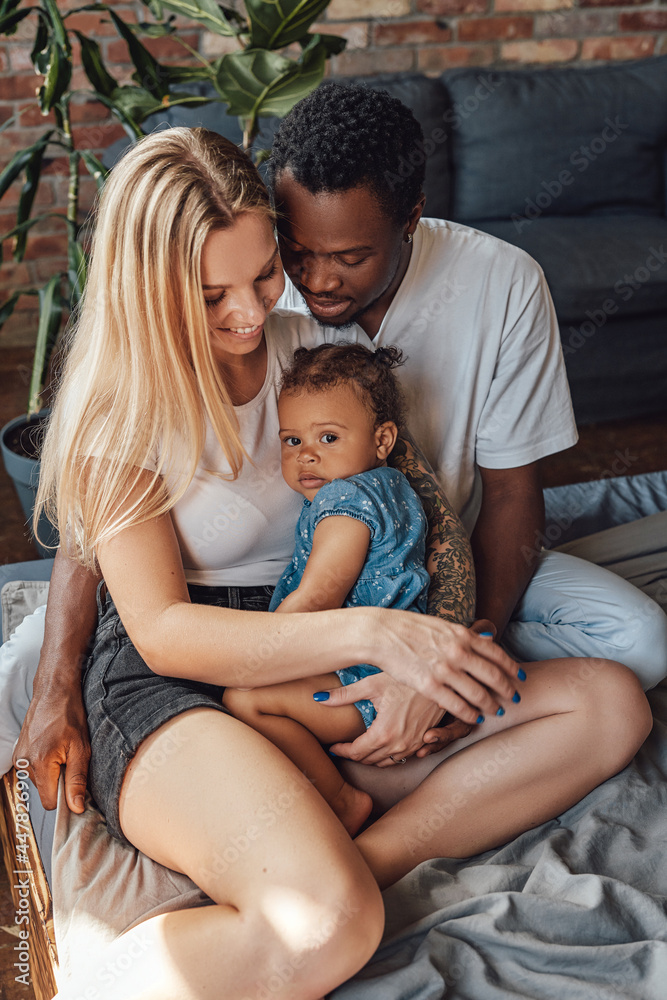 Fototapeta premium Cheerful little girl with her multiethnic parents on bed