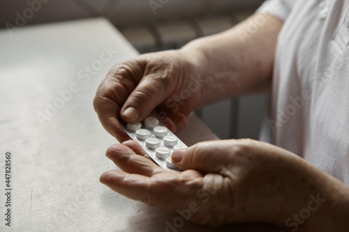 Sad old woman taking pills, health problems in old age, expensive medications. An elderly woman's hands unpacking several pills for taking medication. Grandma takes tablet and drinks a glass of water