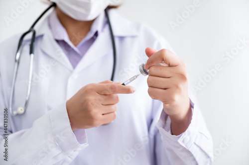 Female doctor wearing a mask stands holds a syringe with a bottle of vaccine for protection Coronavirus19 in a laboratory. Concept of preventing the spread of COVID-19.