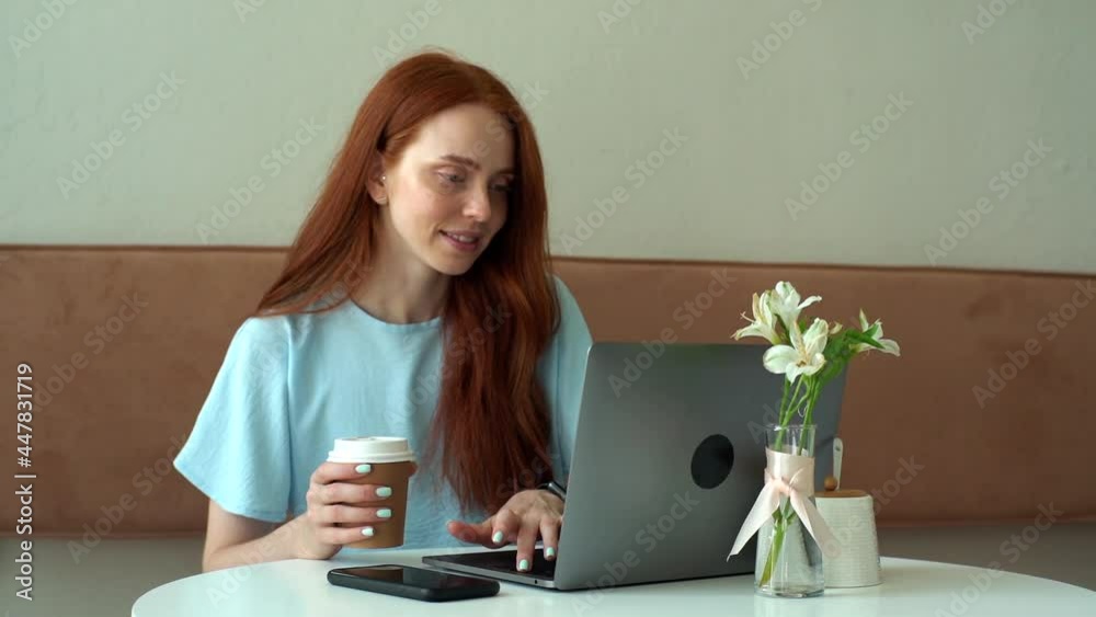 Medium shot of cheerful young beautiful woman typing on laptop and drinking coffee from cup while working remotely at cozy cafe. Portrait of happy female freelancer watching news at laptop screen.