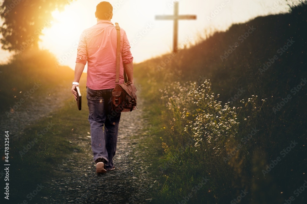 Male holding the bible walking up to the hill towards the cross with a blurred background