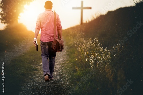 Fotografia Male holding the bible walking up to the hill towards the cross with a blurred b