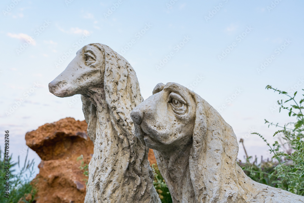 Two sculptures of sad dogs in the garden close-up side view