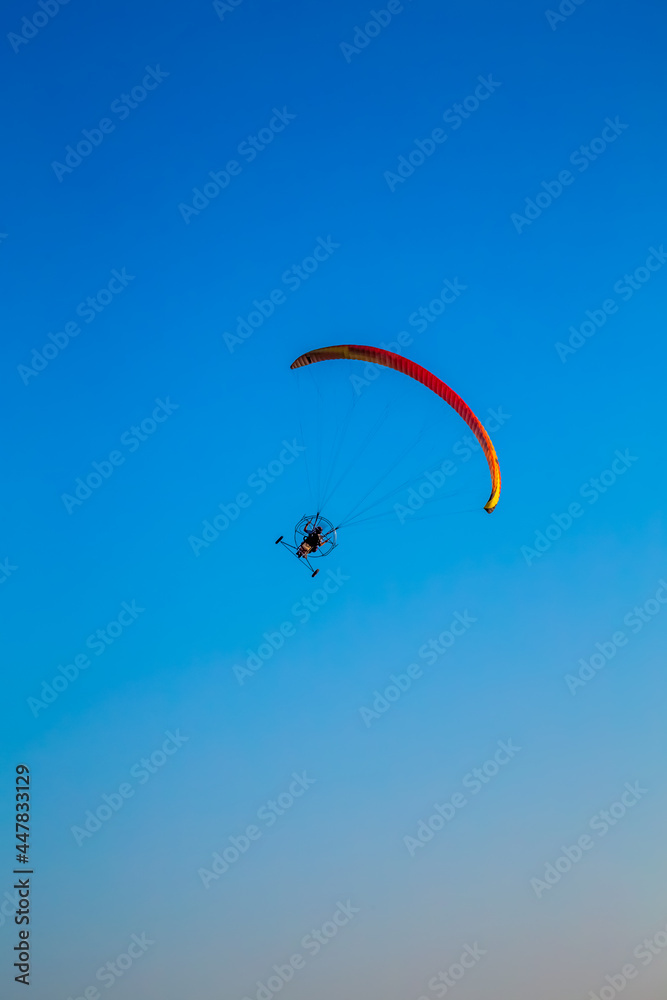 paraglider flying with paramotor on air on evening against the blue sky paraglider flying with paramotor on air on evening against the blue sky