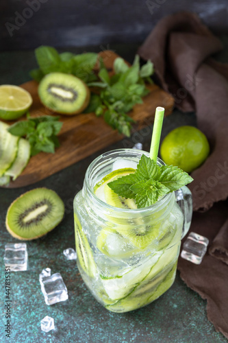 Summer refreshing drink with kiwi, cucumber, lime and ice, mojito or soda with cucumber on a dark stone table.