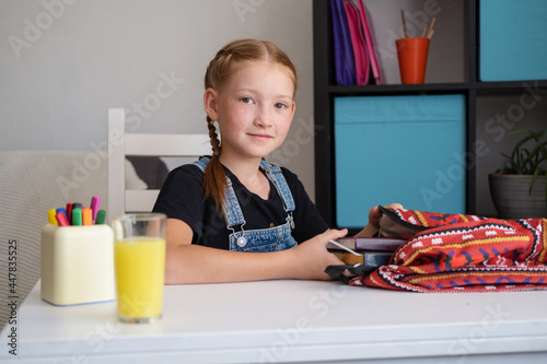 Cute redhead girl packing backpack, preparing for school photo