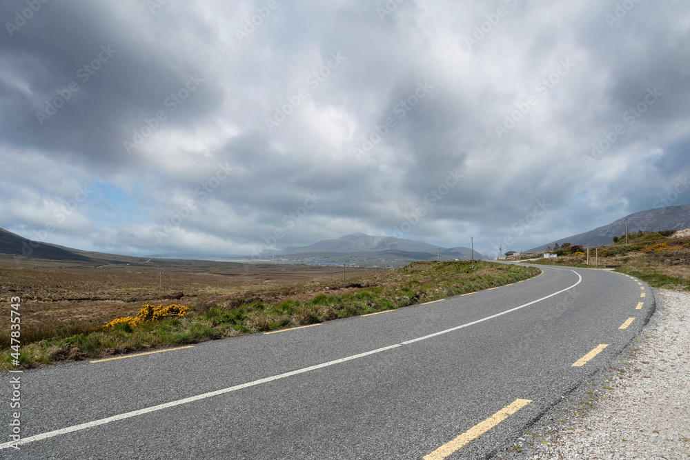 Narrow asphalt road on a warm sunny day, beautiful cloudy sky, nobody. Achill island, county Mayo, Ireland. Travel concept