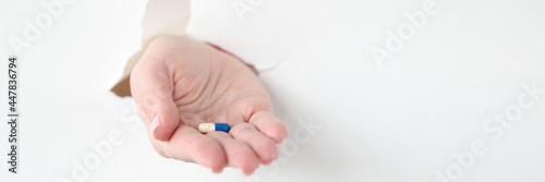 Hand pulling out medicine capsule from torn paper