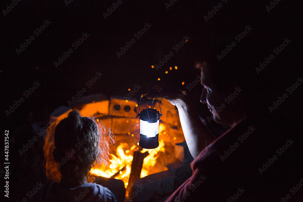 Dad and daughter sit at night by the fire in the open air in the summer ...