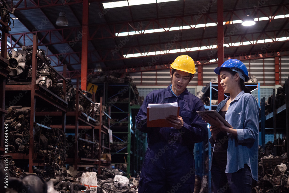 Asian engineer wearing safety helmet holding clipboard with worker in the automotive warehouse. Asian engineer wearing safety helmet holding clipboard with worker in the automotive warehouse.