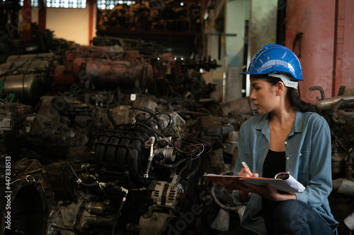 Asian female worker with clipboard and checking old automotive spare parts. Recycle motor factory. 