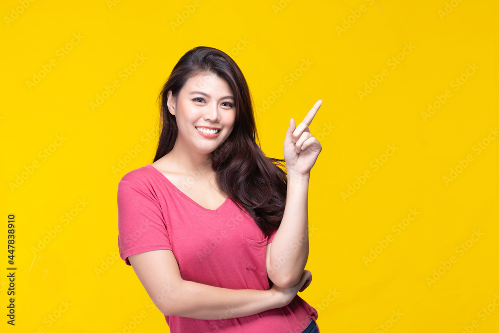 Image of feeling smile and happy. Cheerful young asian woman with brunette long hair in casual shirt smiling with teeth pointing up with index finger to copy space. Female face expressions. Image of feeling smile and happy. Cheerful young asian woman with brunette long hair in casual shirt smiling with teeth pointing up with index finger to copy space. Female face expressions.