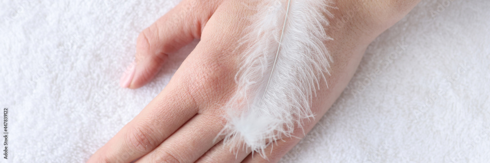 Soft white feather lying on woman hand closeup