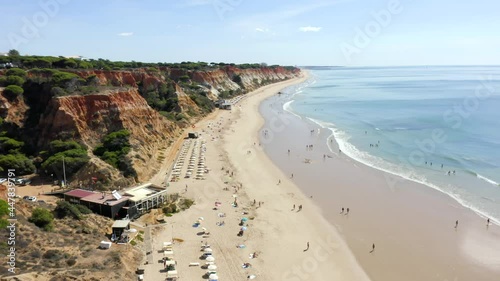 Tourists Enjoying Sandy Beach With Restaurants - Coastal Cliffs And Seascape From Falesia Beach In Algarve, Albufeira, Portugal. - aerial drone photo