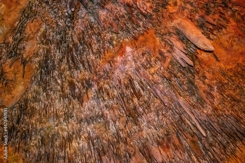 Natural abstract texture with sharp spikes of stalactites on the ceiling of Damlatas cave (Alanya, Turkey). Brown-orange pattern of stone mineral formations