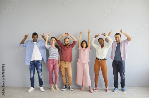 Casual portrait of happy diverse multiethnic people standing against light grey studio wall background showing various non verbal body language hand gestures like OK, thumbs up, rock n roll horn sign photo