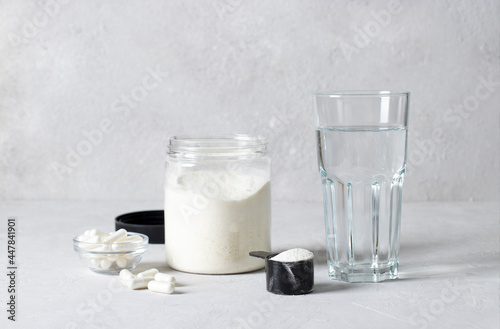 Collagen powder in a jar and measuring spoon, collagen capsules and a glass of water on light gray background. Healthy and antiage concept